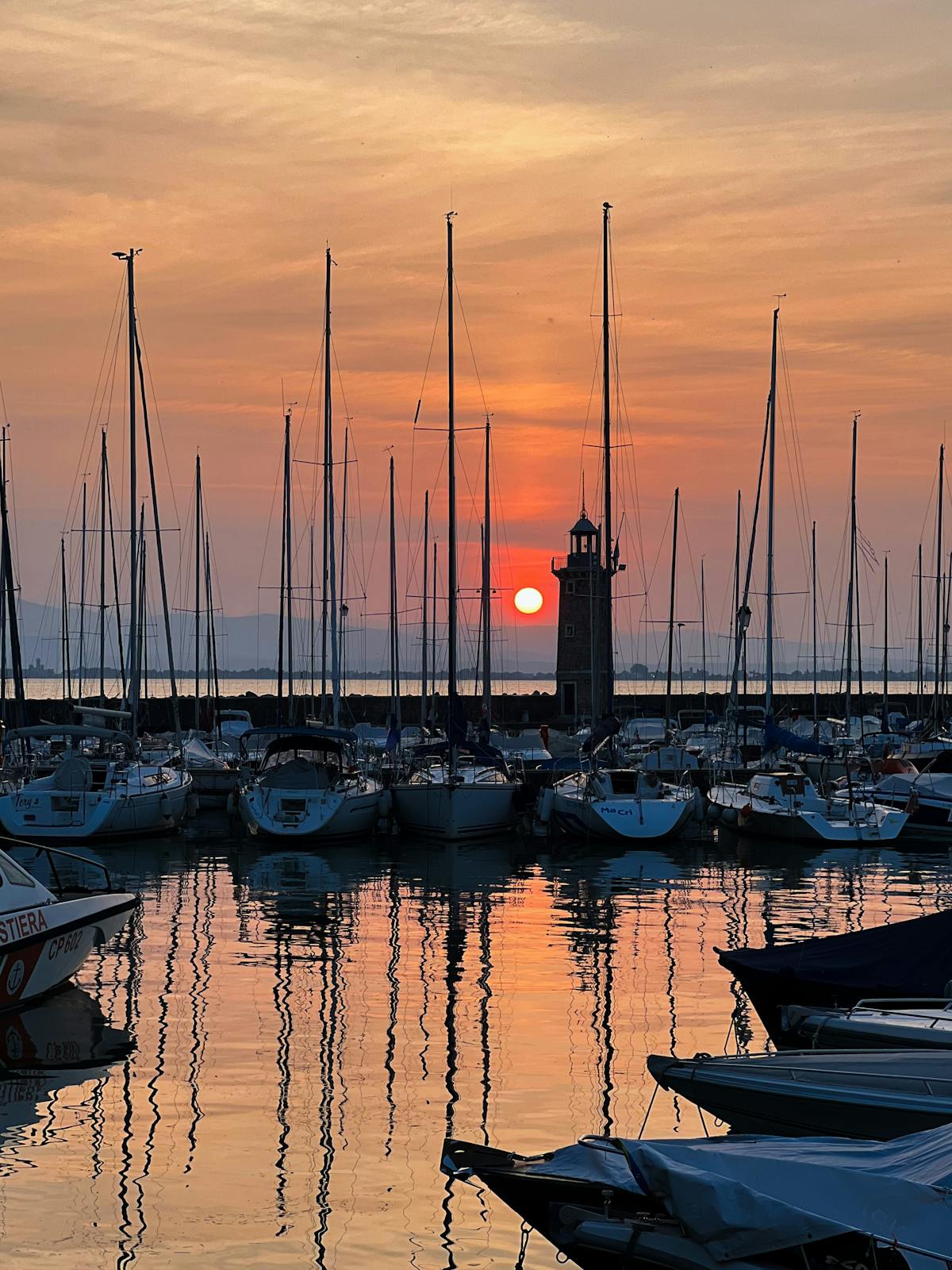 The old harbour of Desenzano del Garda at sunset with moored sailboats and the iconic lighthouse