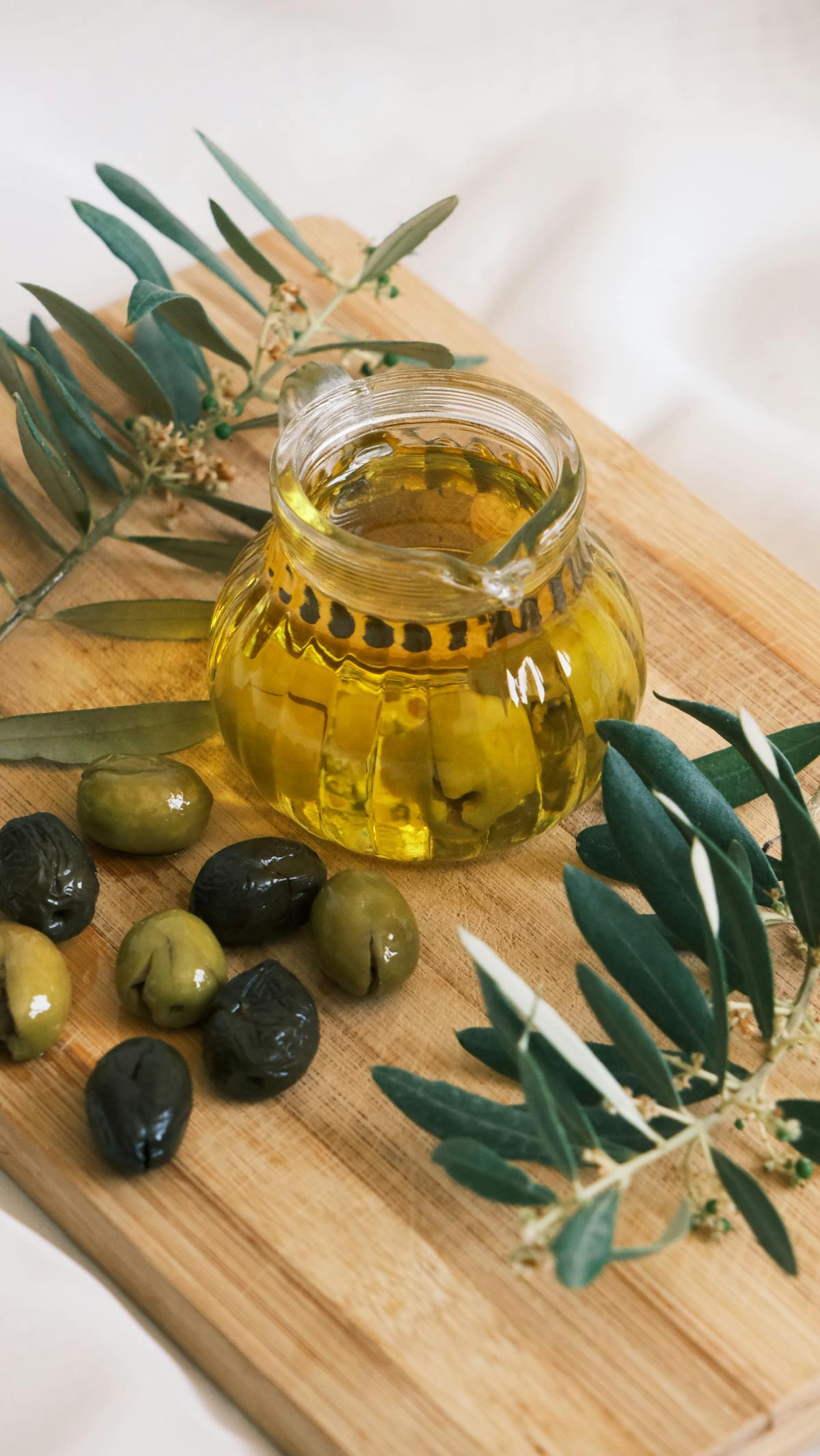 A bottle of pale green Lake Garda olive oil on a wooden table with olives beside it
